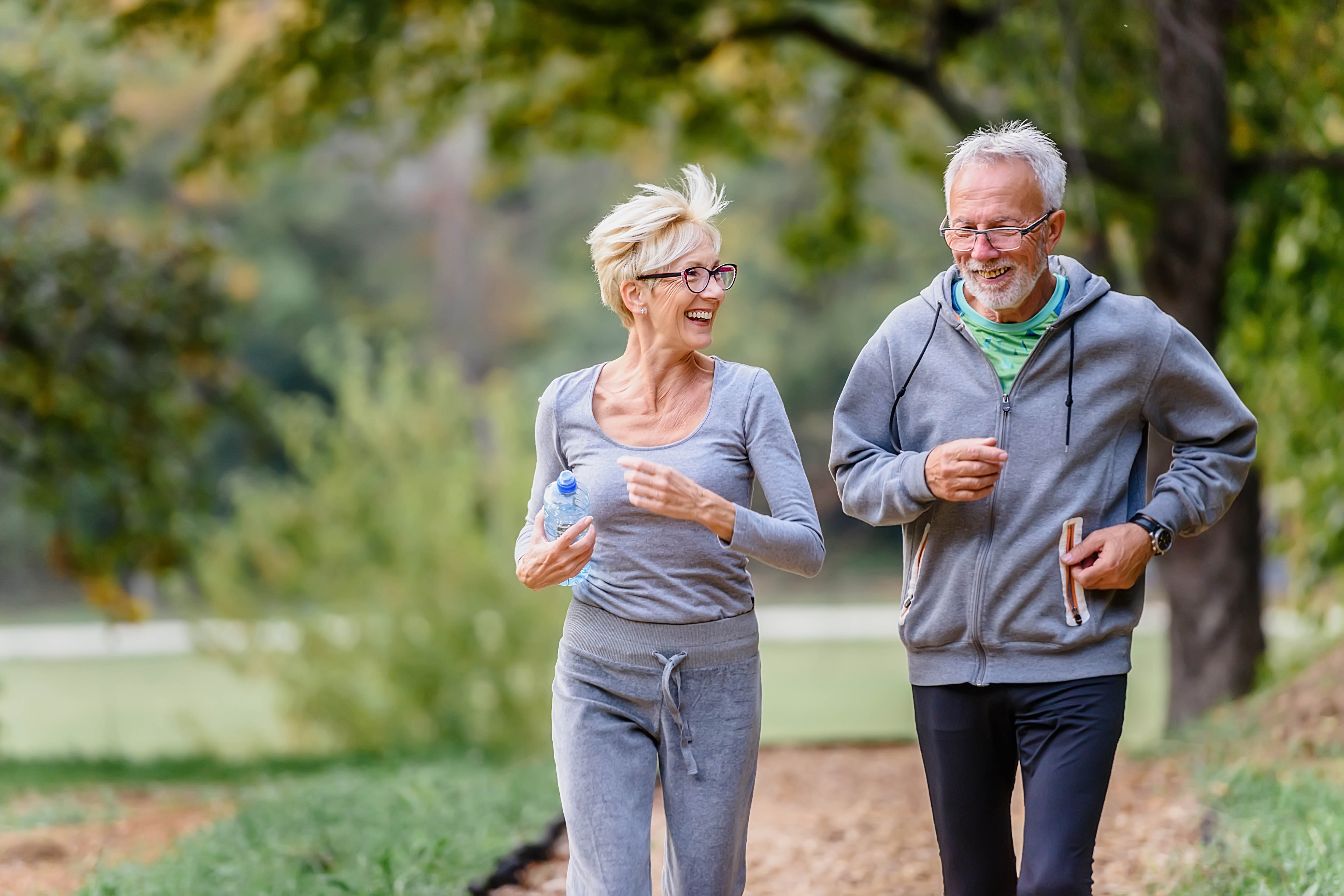 Older couple out for a run along a trail, trees blurred out in the background